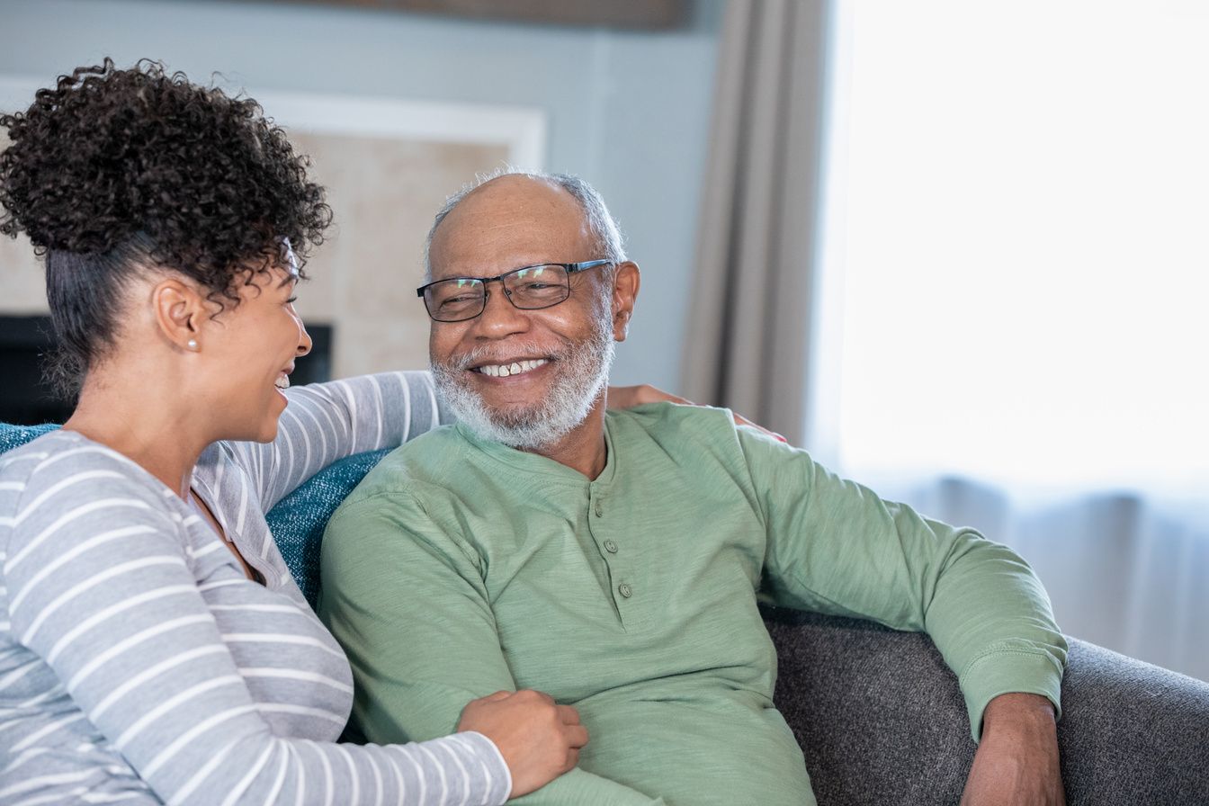 An older man laughing with a younger woman on a sofa